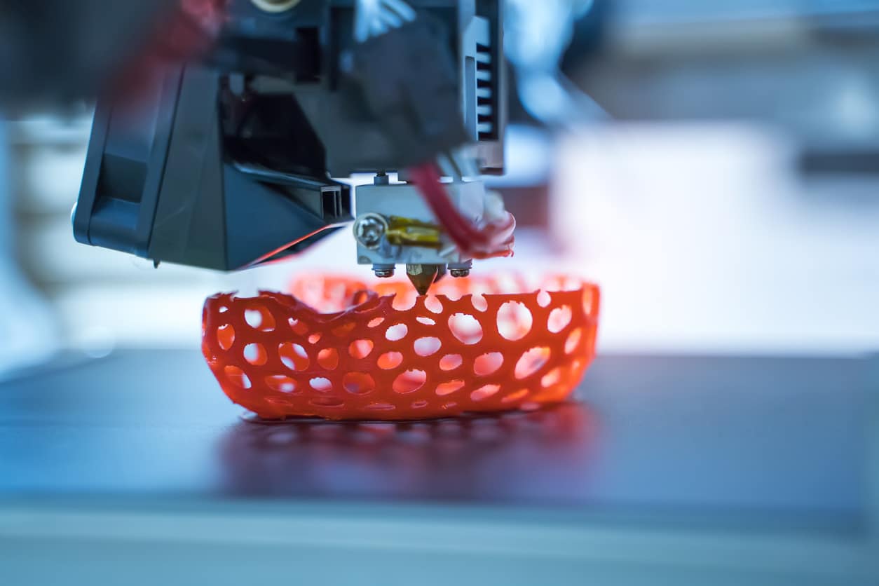 Close-up of a 3D printing machine building a red bowl.