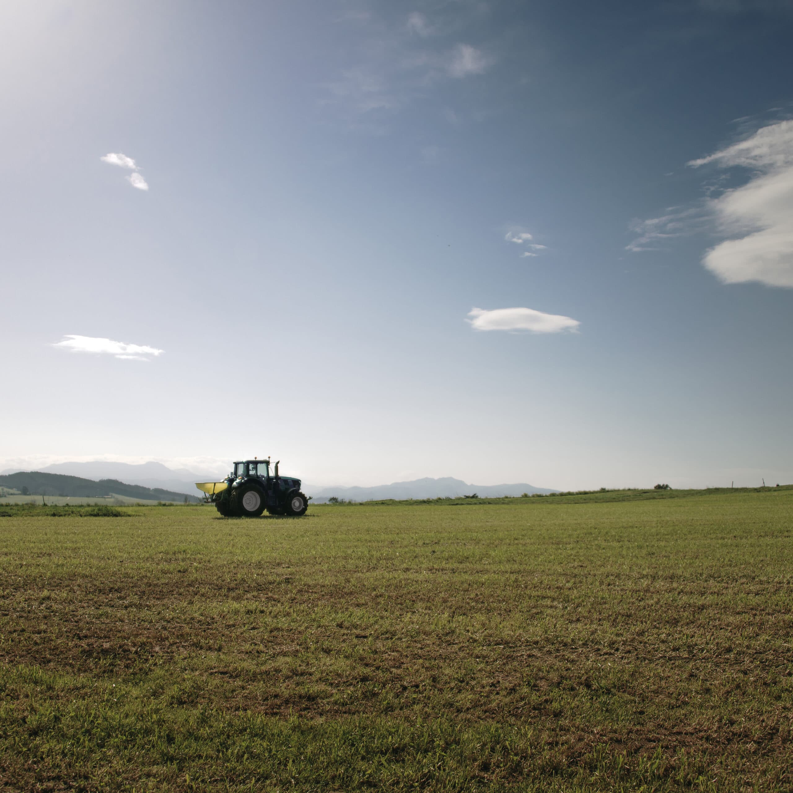 A tractor fertilizing a green field under a clear blue sky.