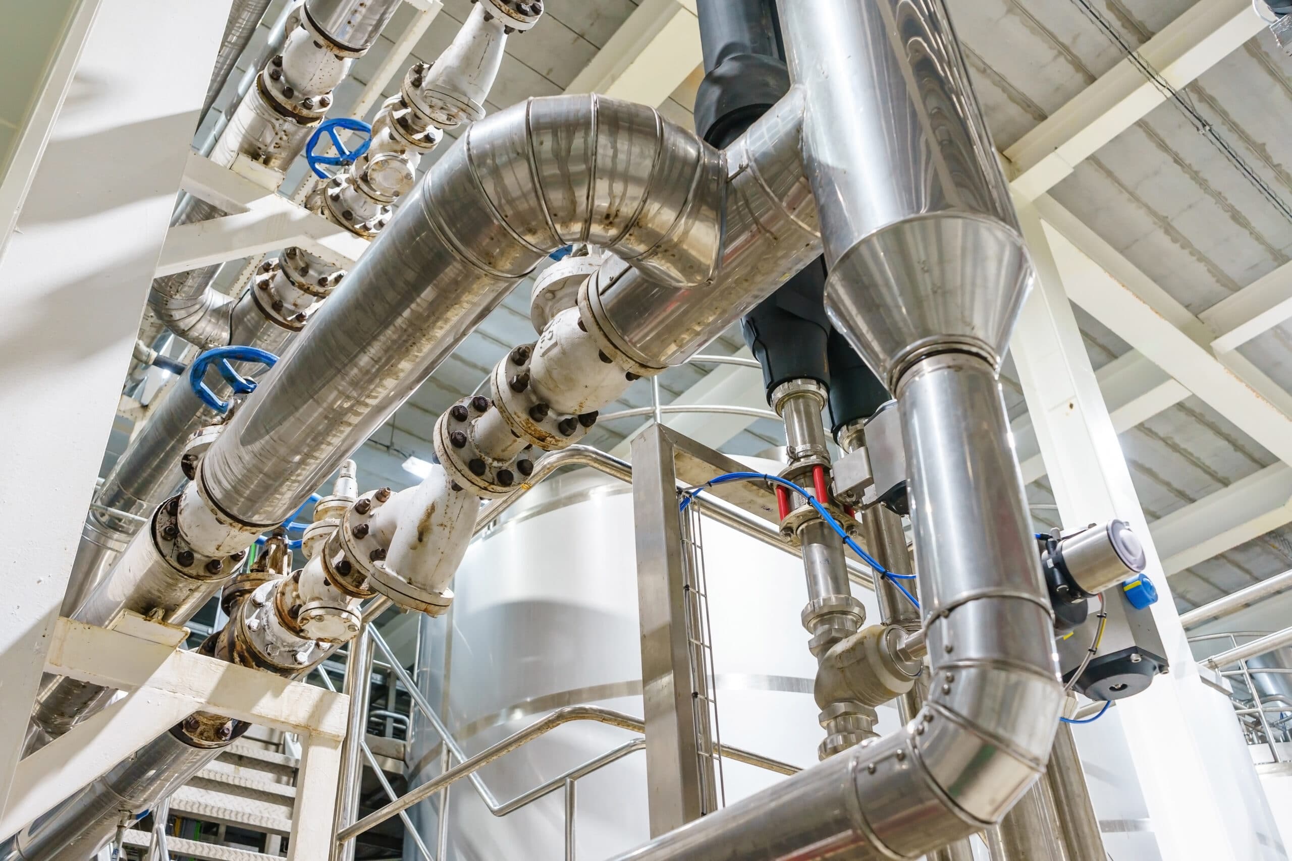 Interior of an industrial plant with machinery, steel pipelines, valves, and ladders.